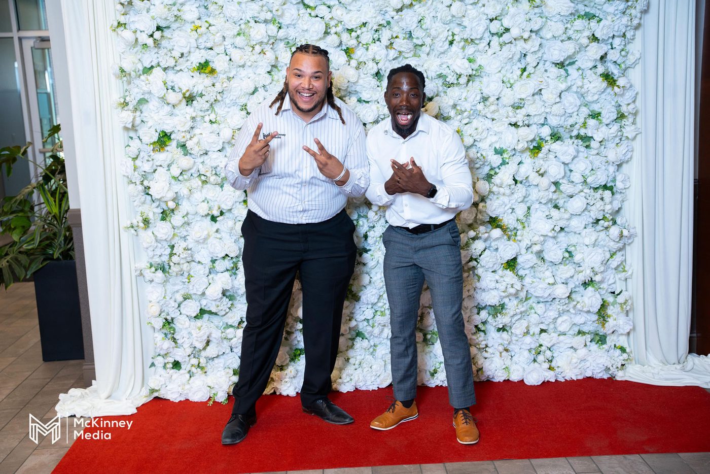 Two members smiling in front of a white flower wall