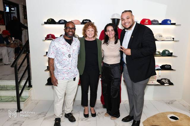 Four guests in front of a hat display wall at Headshot Happy Hour
