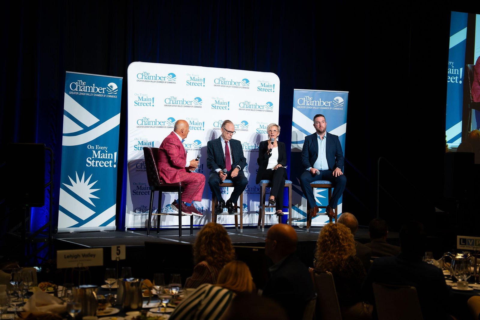 Panelists appear on a large screen at a conference