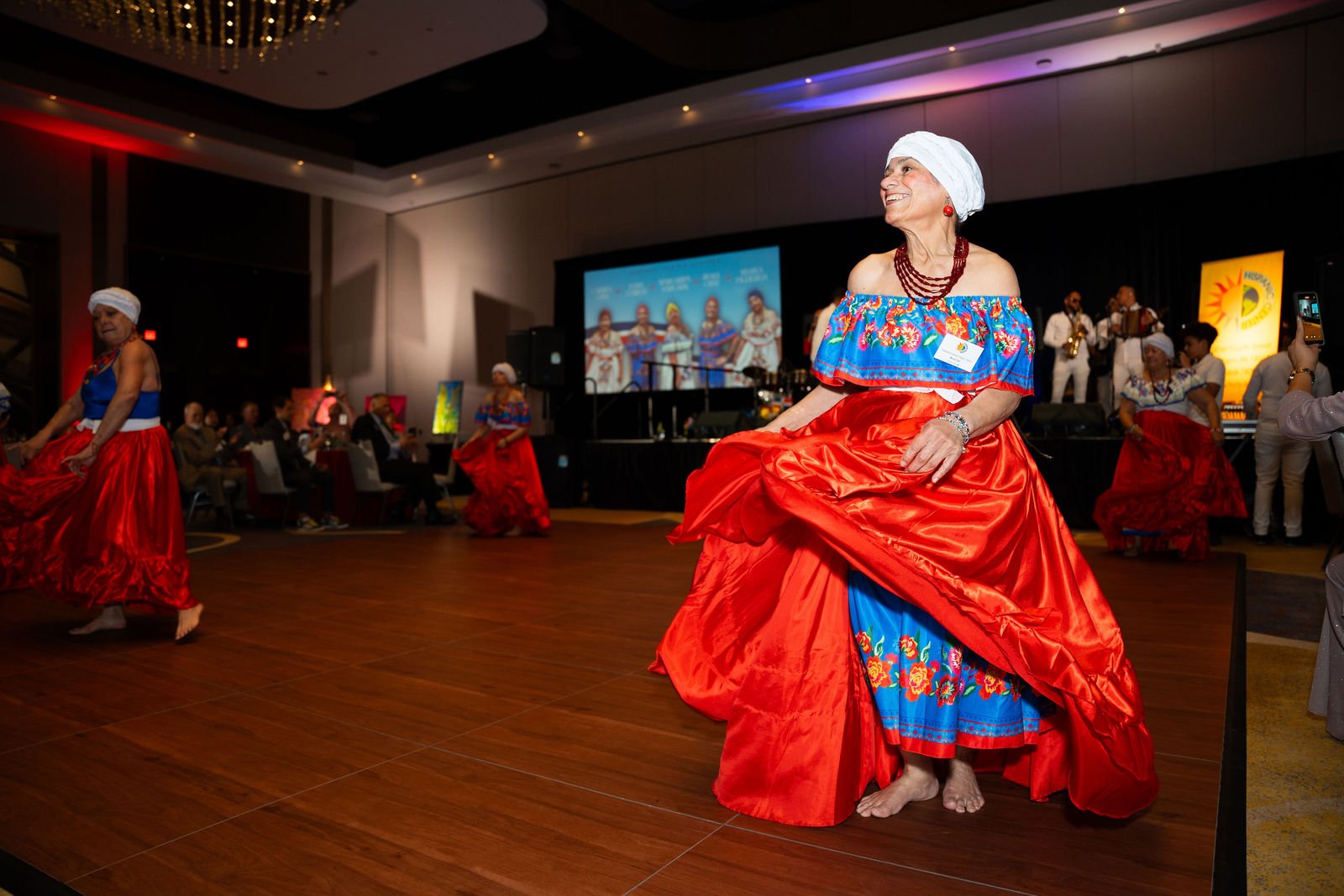 A performer in a colorful dress appears on stage at an event