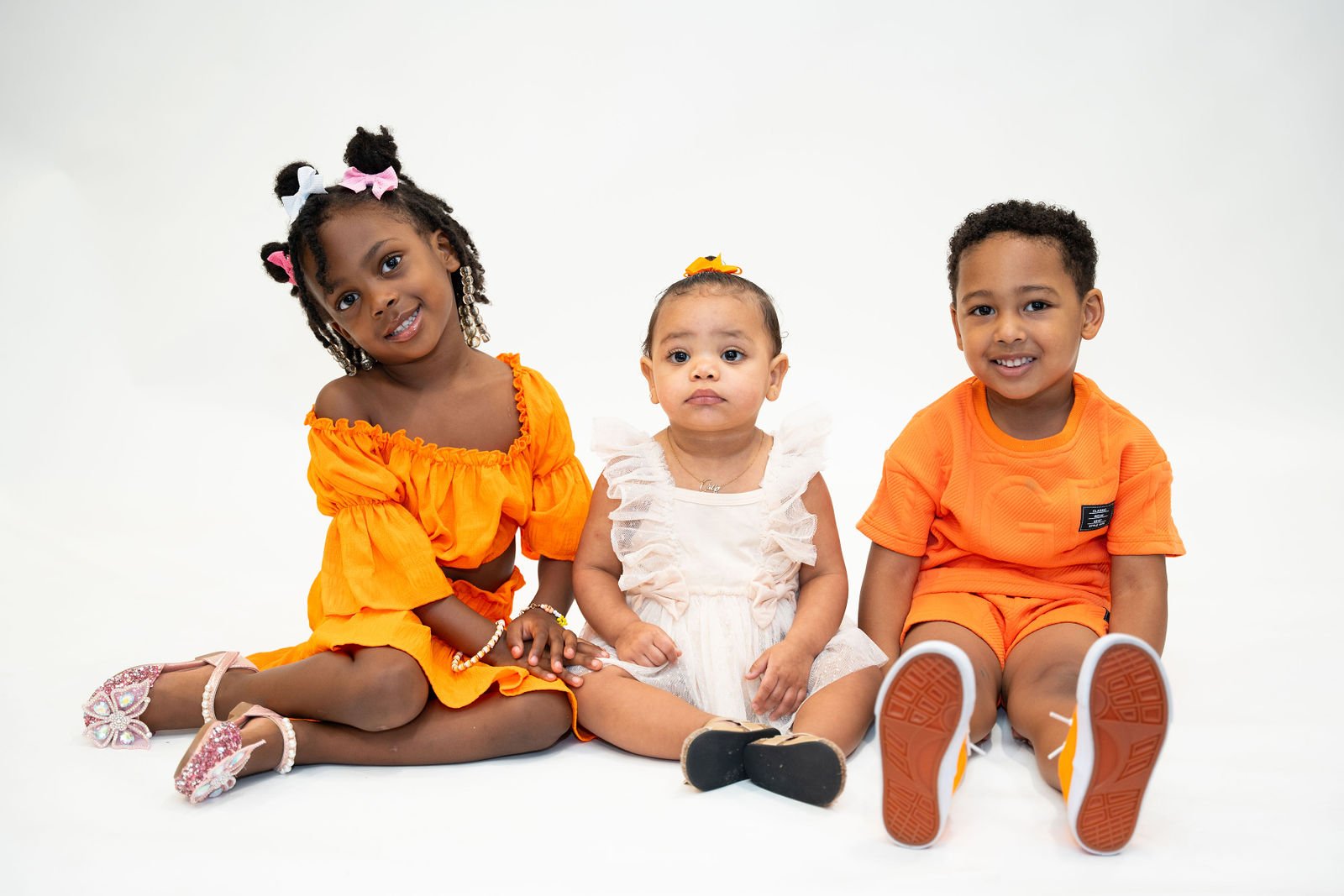 Three young children sit together in matching orange outfits