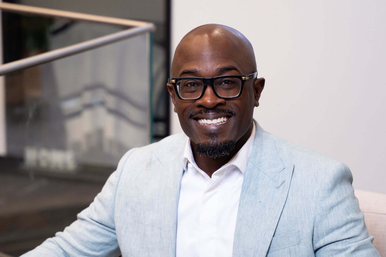A smiling man in glasses and a light jacket poses for a headshot