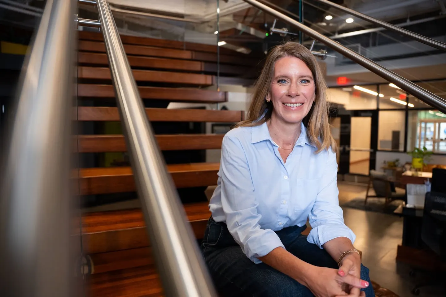 A woman sits beside a staircase in a modern office
