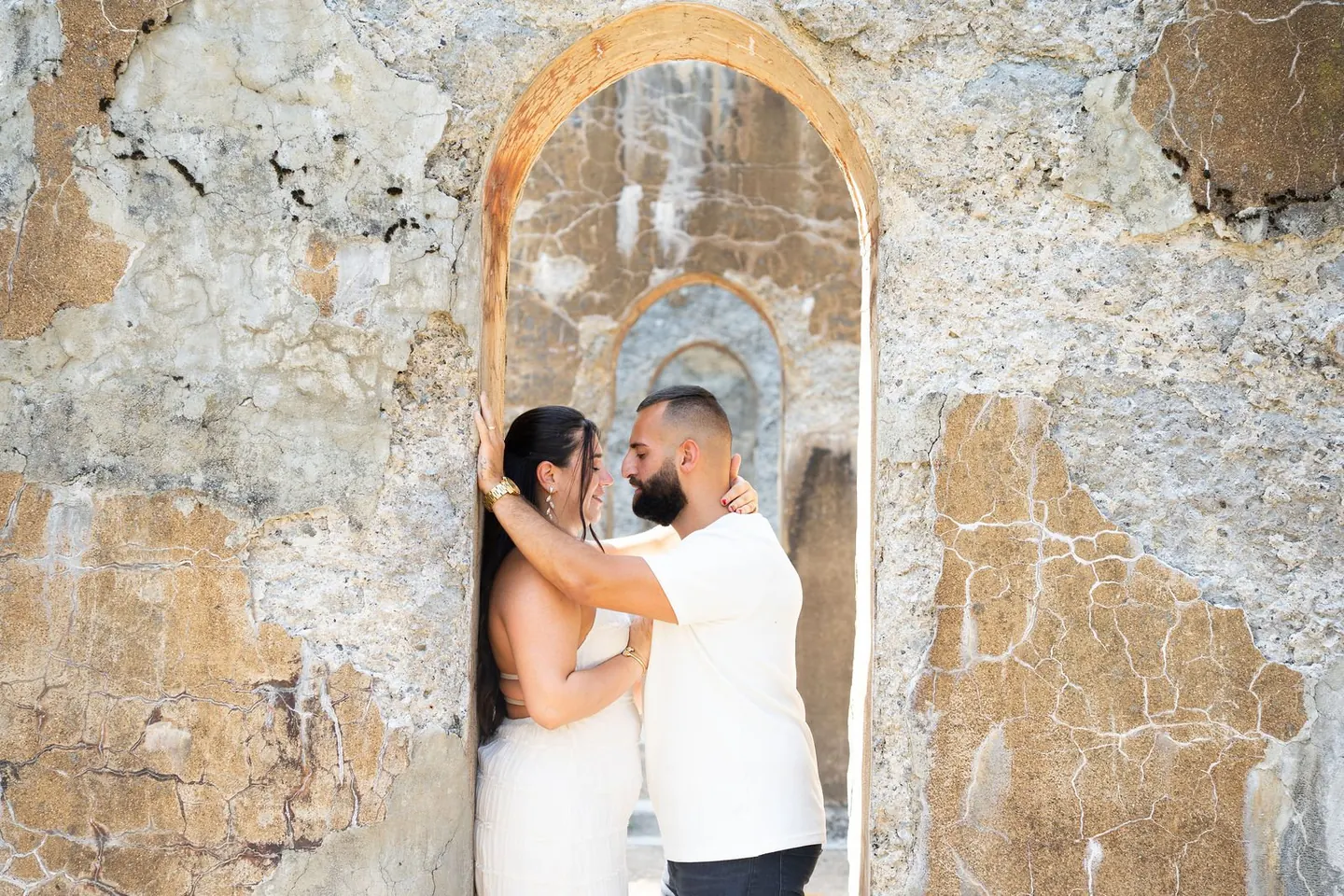 A couple embraces in front of a stone wall