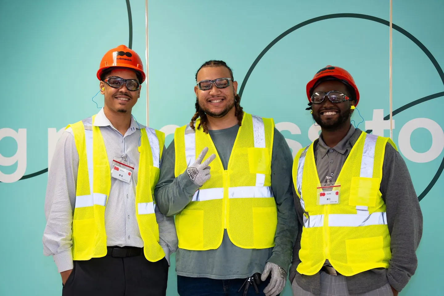 Three people in safety vests pose at a production location