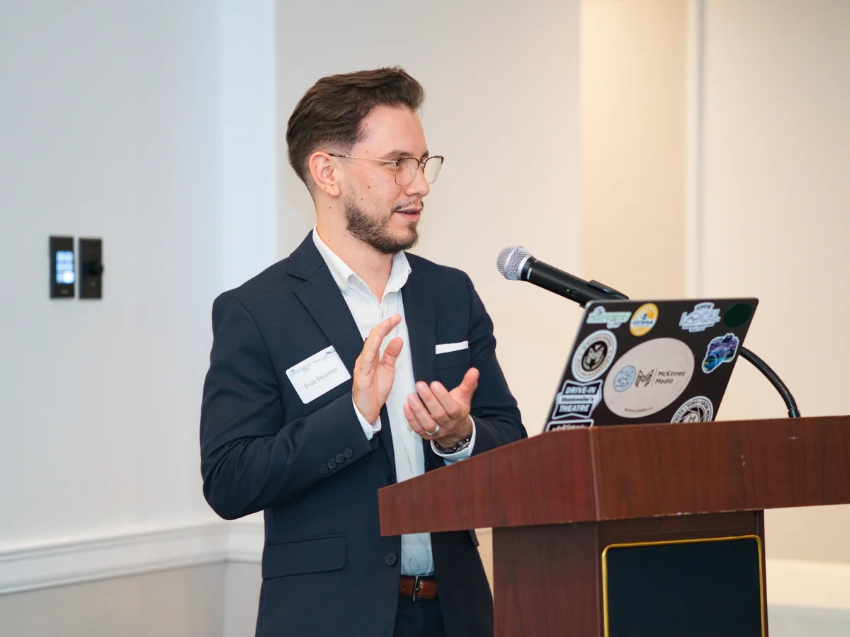 A presenter speaks beside a laptop and microphone at Headshot Happy Hour: Business Finance